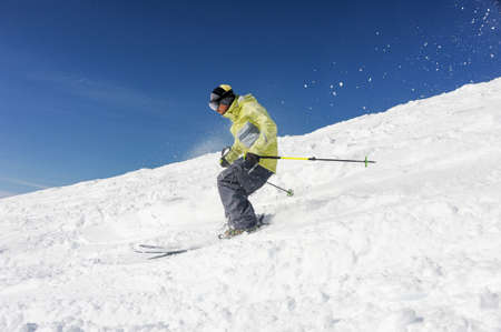 Skier man, dressed in yellow and grey sportswear, running down the mountain hill on the background of wonderful Gudauri, Georgiaの写真素材