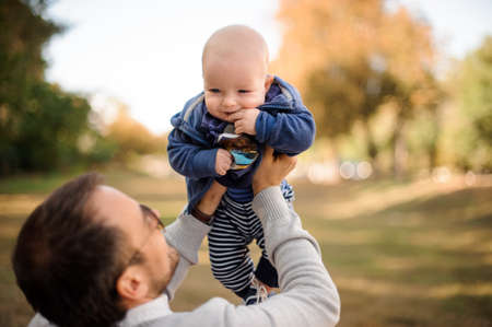 Father playing and having fun with a cute baby son in the beautiful autumn parkの写真素材