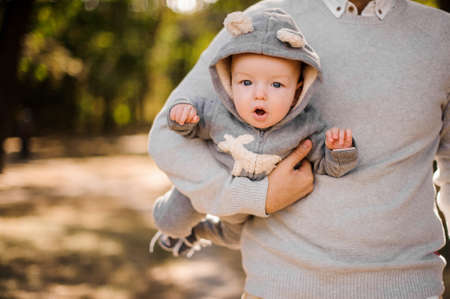 Father walking in the park and holding a cute baby son dressed in a romper under armの写真素材