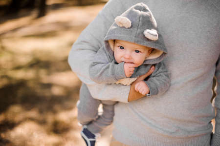 Father walking in the park and holding a cute little son dressed in a romper under his armの写真素材
