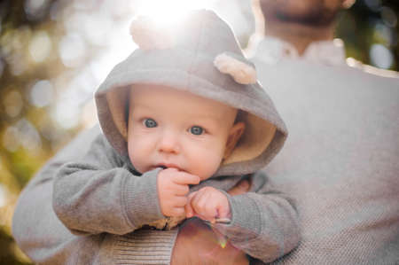 Portrait of a cute baby boy in father hand against the background of green trees and sun raysの写真素材