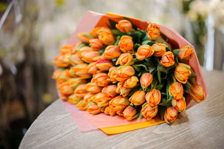Large and beautiful bouquet of bright orange tulips wrapped in a pink and orange paper on the tableの写真素材