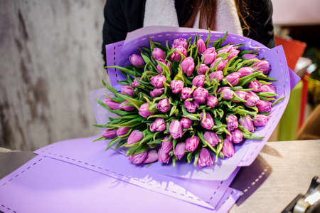Large and beautiful bouquet of bright purple tulips wrapped in a purple paper on the tableの写真素材