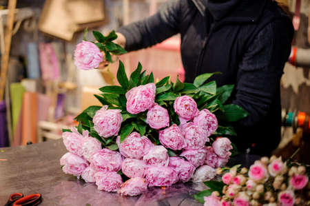 Professional florist making a bouquet of fresh and bright pink peonies in a flower shopの写真素材