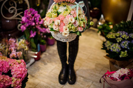 Woman holding a big wicker basket with tender pink roses and other colorful flowers in a flower shopの写真素材