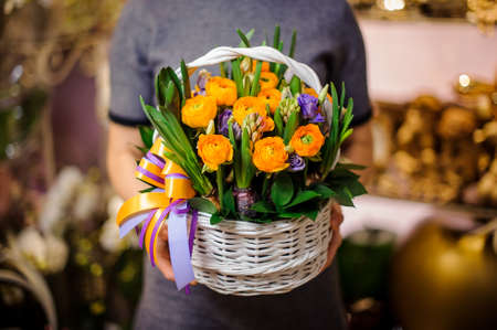 Woman holding a white wicker basket with flowers consisting of orange and purple ranunculus in a flower shopの写真素材