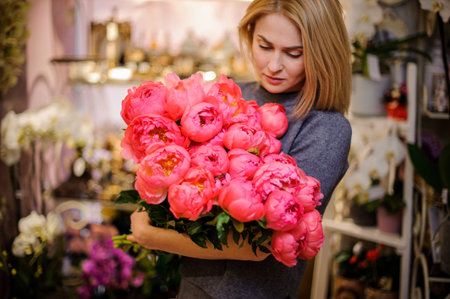 Blonde woman holding a big bouquet of bright pink peonies on the background of a flower shopの写真素材