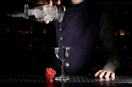 Barman pouring alcoholic drink into the elegant cocktail glass near the red rosebud on the bar counterの写真素材