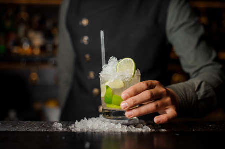 Barman hand holding a glass with a fresh mojito cocktail with sour and sweet taste on the bar counter among iceの写真素材