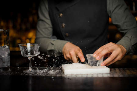 Barman preparing a large rectangular piece of ice n the plastic desk for making cocktail on the bar counter among bar equipmentの写真素材