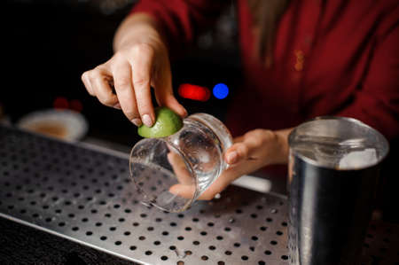Female barman hands rubbing a cocktail glass with fresh green lime juice on the bar counterの写真素材