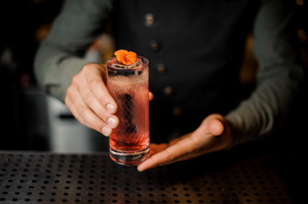 Bartender hand holding a glass with summer light sour cocktail with pink peach liquor decorated with...