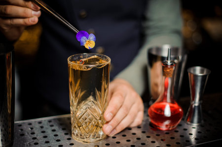 Bartender decorating a sweet and fresh alcoholic cocktail with a little purple flower on the bar...