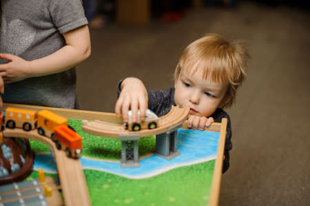 Cute little boy is playing with toy wooden train in the playing room on focusの写真素材