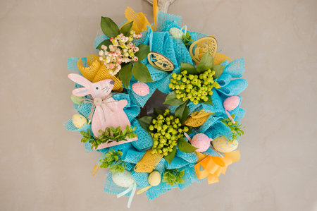 Blue and yellow wreath with flowers, ribbon, eggs and small bunny rabbit shape for Easter celebrations on the wallの写真素材