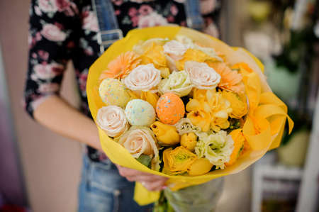 Florist holding a bright yellow Easter bouquet of flowers decorated with colorful eggs and ribbonの写真素材