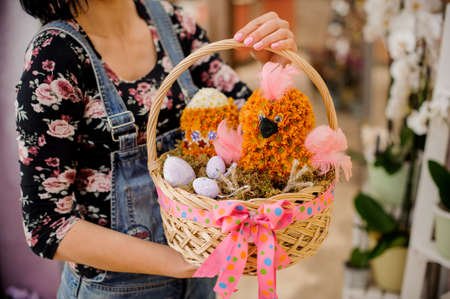 Woman holding an Easter gift consisting of wicker basket with chicken and egg shape flowers in the nestの写真素材