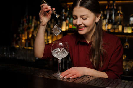 Smiling female barman putting ice cubes into a glass making a fresh and tasty Aperol syringe cocktailの写真素材