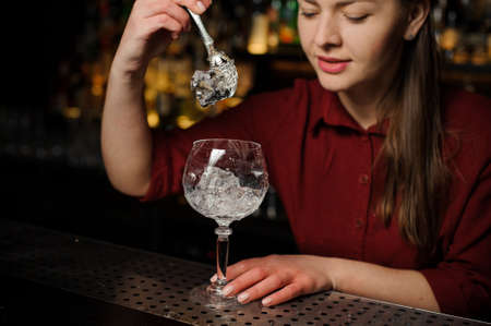 Beautiful female barman putting ice cubes into a glass making a fresh and tasty Aperol syringe cocktailの写真素材