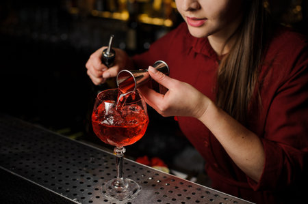 Woman bartender pouring bitter into a glass for making a fresh and tasty Aperol syringe cocktail on...