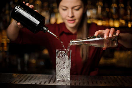 Young female barman poting gin and sweet syrup into a glass for making a fresh summer cocktailの写真素材