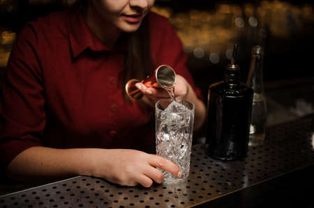 Side view of bartender pouring some gin into a cocktail glass for making a bitter fresh summer drinkの写真素材
