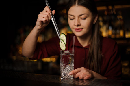 Young woman bartender making a fresh and tasty alcoholic cocktail with gin and cucumber slices