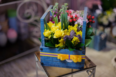Beautiful blue wooden box of the crimson, white and yellow flowers decorating with a green leaves and red berriesの写真素材
