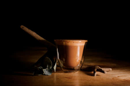 Transparent cup filled with hot and aromatic coffee drink with milk near the dried tree branch on the tableの写真素材