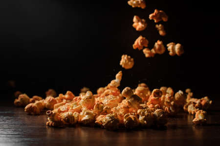 Portion of a delicious popcorn falling down on the wooden table on the dark backgroundの写真素材