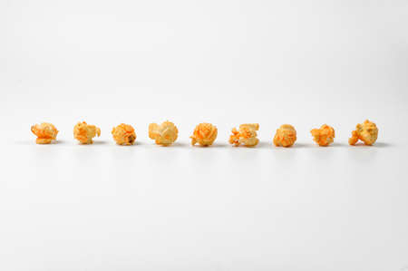 Nine pieces of a delicious yellow popcorn lying on the white background in a rowの写真素材