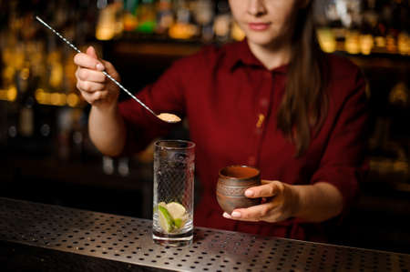 Female bartender putting a cane sugar into a glass with spoon at the steel bar counterの写真素材