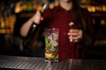 Delicious cocktail on the background of barman girl which holding a bottle with liquor and measuring pileの写真素材