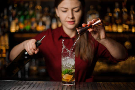 Female bartender pouring out a transparent alcoholic drink from the measuring pile with splash for preparing a delicious fresh cocktailの写真素材
