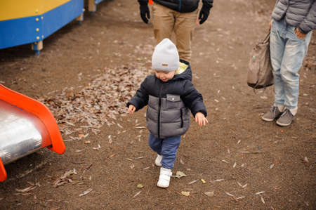 Little boy dressed in warm clothes walking with parents in the autumn park on the cloudy dayの写真素材