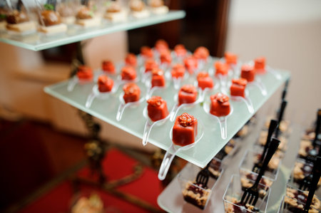 Set of salty small appetizers in a red glaze decorated with sun-dried tomato served on the glass...