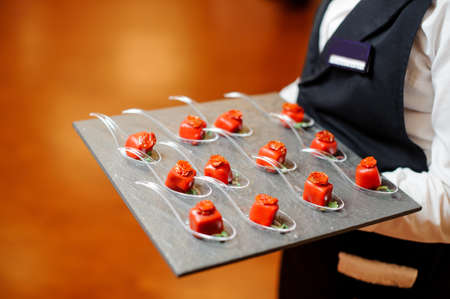 Waiter serving a plate with salty small appetizers in red glaze decorated with sun-dried tomato and microgreensの写真素材