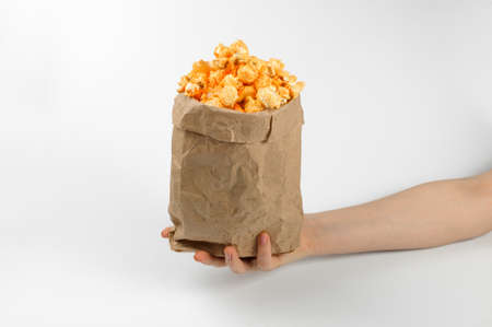 thin female hand holds a craft package of large air grains of yellow delicious roasted popcorn on a white backgroundの写真素材