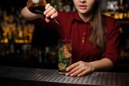 cute barmaid in a red dress prepares a mojito in a crystal glass, adding dark rumの写真素材