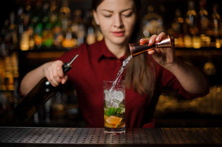 barmaid completes the preparation of the mojito in a crystal glass, adding a white rum, against the bar counter in the barの写真素材