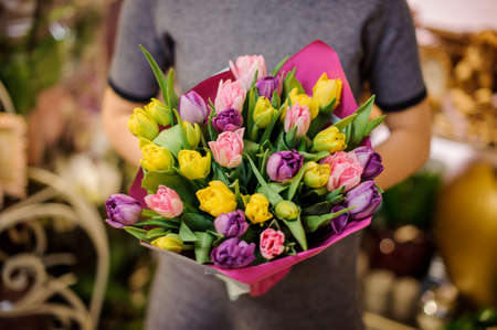 Girl holding in her hands a wonderful bouquet of pink, yellow and violet tulips decorating with a green leavesの写真素材