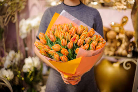 Girl holding in her hands a wonderful bouquet of orange tulips decorating with a green leavesの写真素材