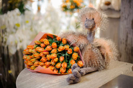Wonderful bouquet of orange tulips decorating with a green leaves wrapping in the orange paper lying on the tableの写真素材