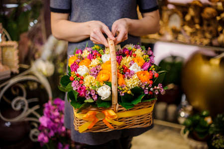 Girl holding in her hands a beautiful basket consisting of multi colored spring flowers decorated with yellow bowの写真素材