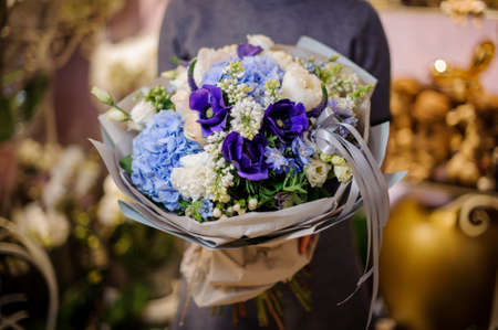 Girl holding a beautiful bouquet of white, blue and violet flowers wrapped into a gray paperの写真素材