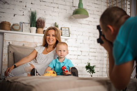Father taking a photo of his smiley wife and little son, who sitting on the bed