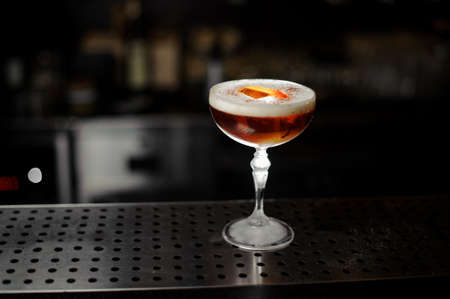 Fresh delicious decorated brown cocktail with a white scum standing on the steel bar stand under the spotlightの写真素材