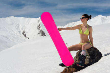 Young sexy woman dressed in a swimsuit sitting on the stone with a board among high mountainsの写真素材