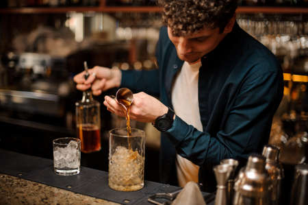 Young barman pouring a sweet syrup into a jar with ice making an alcoholic drink on the bar counterの写真素材