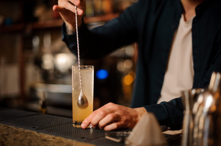 Barman hand stirring a fresh and sweet orange summer cocktail with a spoon on the bar counter